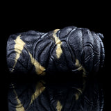 Angled view of the black textured vibrating stroker with gold accents and segmented grip