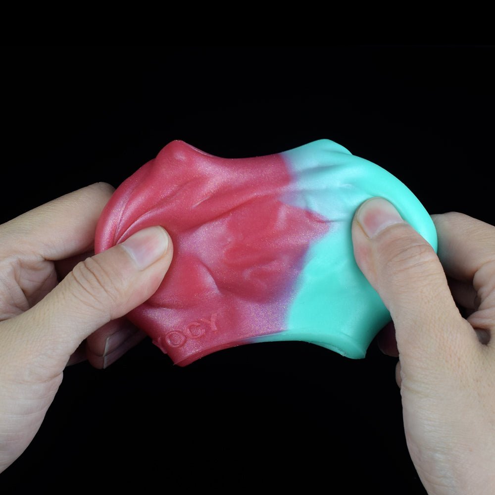 Penis-Sleeve Extender in den Händen, breite Öffnung, rosa-türkis mit Drachenstruktur