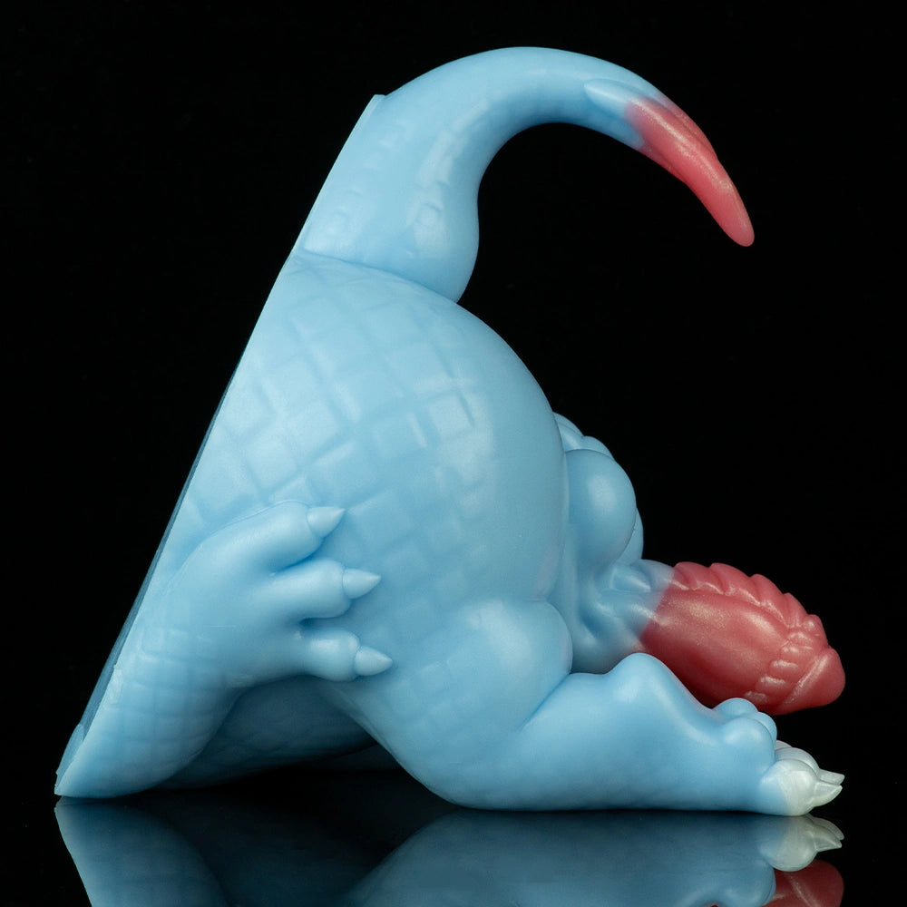 Light blue dragon toy lying with arched back and pink head crest, close side view