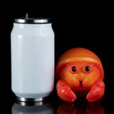 Orange-red squeeze toy crab next to a white cup, front view