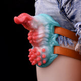 Grinder strap-on toy with red-blue bumpy surface and tan straps on jeans