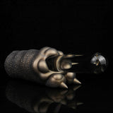 Bronze textured clawed hand reaching toward a small dark cylindrical object