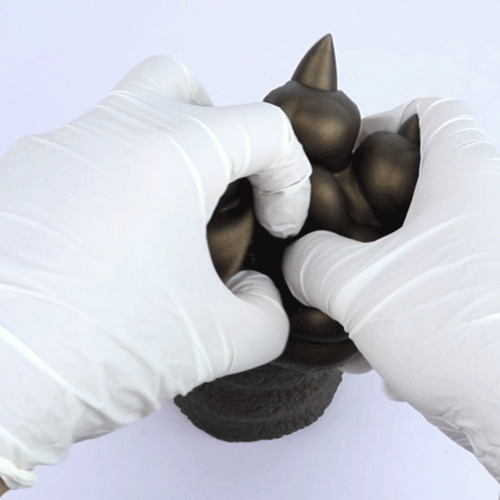 Bronze textured clawed hand held by two white-gloved hands