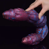 Dildo mit Kopf und Ringdetail, lila-blau schuppig, Hand hält das spitz zulaufende Ende.