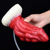 Hand holding red dragon anal plug with white base and clear hose attachment