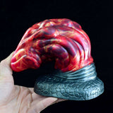 Red dragon butt plug held in hand; dark scaly base and curled patterned body