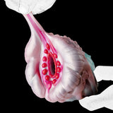 Alien Fleshlight with red-lined inner cavity as gloved hands hold it from the side.