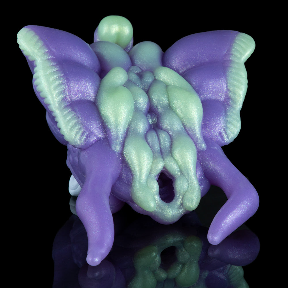 Purple and green alien figurine with open mouth and horned head, lying down