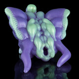 Purple and green alien figurine with open mouth and horned head, lying down