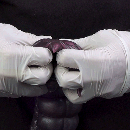 Purple alien creature toy held by white gloves, curled claws and glossy surface