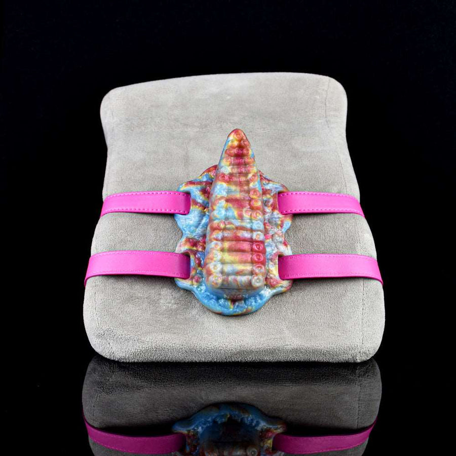 Tentacle grinder toy on gray cushion with rainbow tentacle detail and pink straps