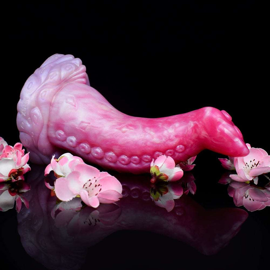 Curved octopus-tentacle butt plug lying on surface, translucent pink tentacle with suction-like textures.