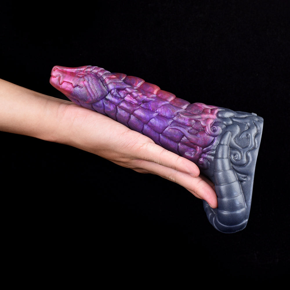Penis extender with purple and pink dragon-scale texture and gray base, held in hand