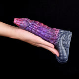 Penis extender with purple and pink dragon-scale texture and gray base, held in hand