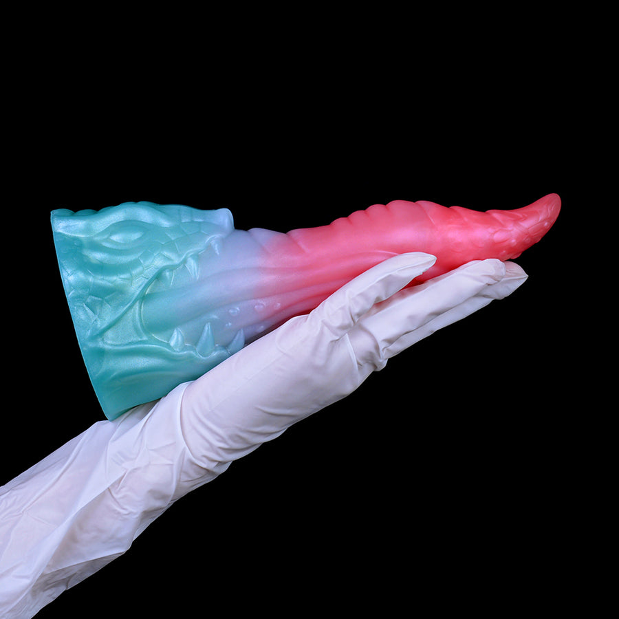 Pink and teal dragon-shaped sex toy resting on white-gloved hand.