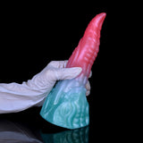 Gloved hand holds pink tip and light-blue textured base of dragon-style dildo.
