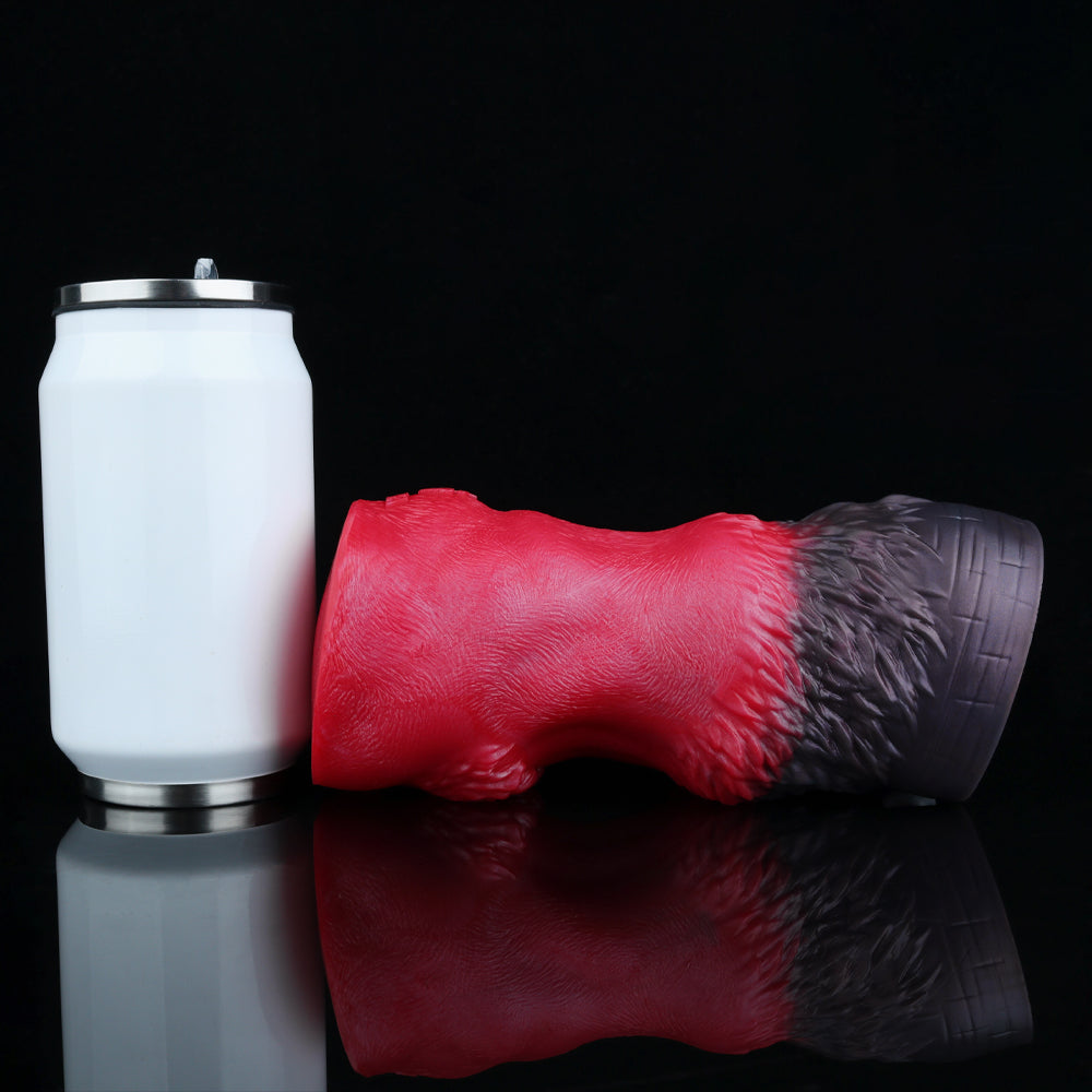Red and black textured pleasure toy lying beside a white accessory container.