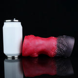 Red and black textured pleasure toy lying beside a white accessory container.