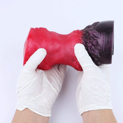 Red and black pleasure toy being held by gloved hands for fit demonstration.