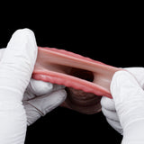 Textured pink cock sleeve/penis sheath held open in white gloves, translucent fabric