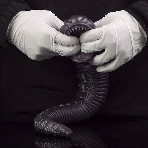 Snake creature toy held by white-gloved hands, dark purple coiled body and open jaw