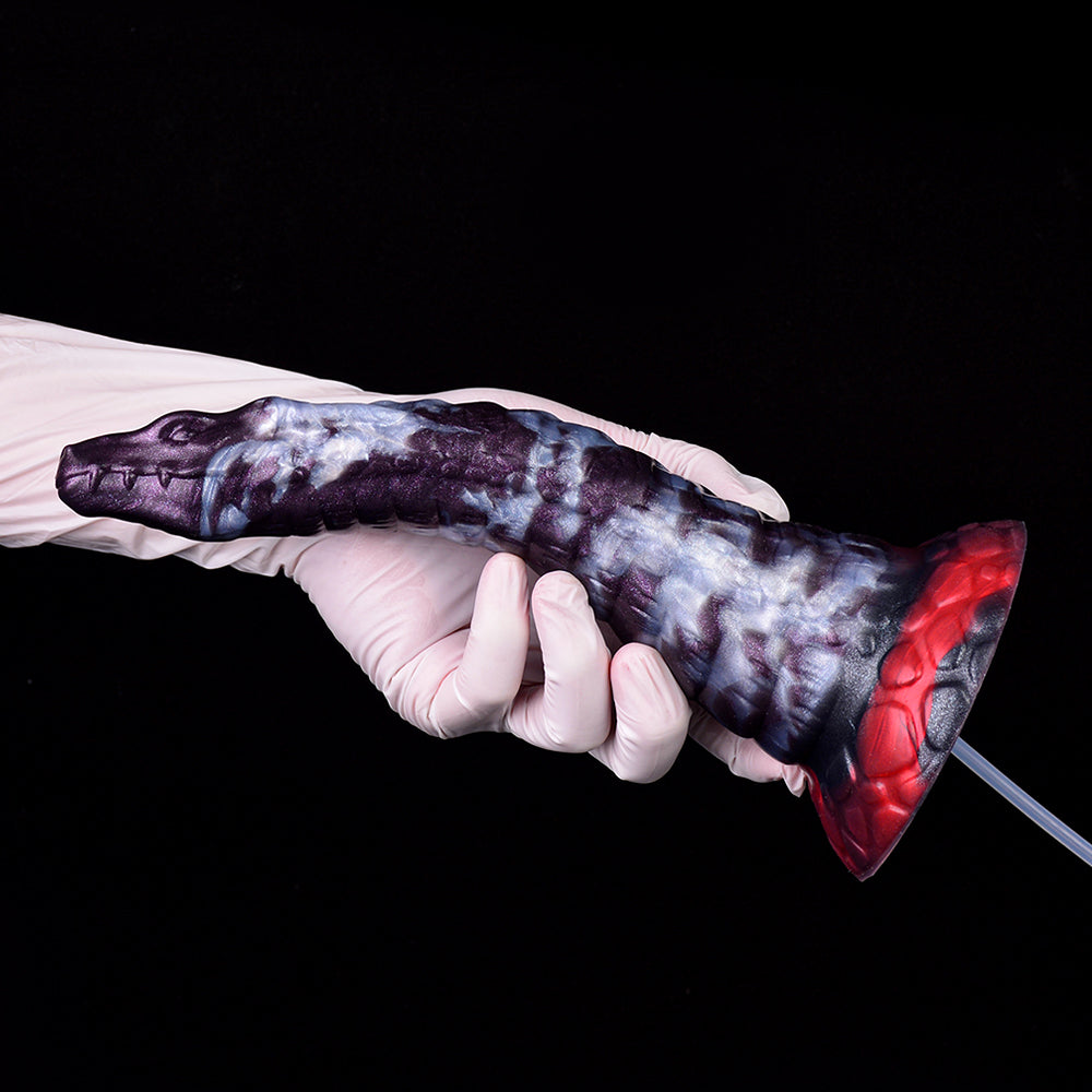 Gloved hand holding purple-and-white dildo with red base and clear hose