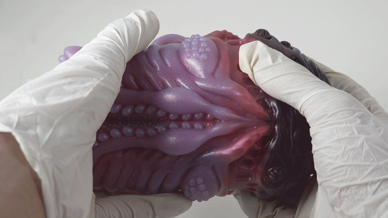 Purple hand-shaped resin sculpture held by white-gloved hands