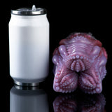 Pink and dark silicone octopus-shaped sex toy beside a white cylindrical holder