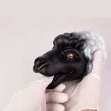 Animal figurine held by gloved hands, black-and-white mane, orange eye, side angle