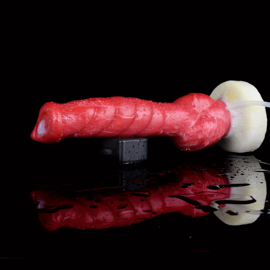 Red textured dildo lying with white base and clear tube, shown with reflective surface.