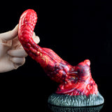 Hand holding curved red monster tongue anal dildo with textured blue-gray base
